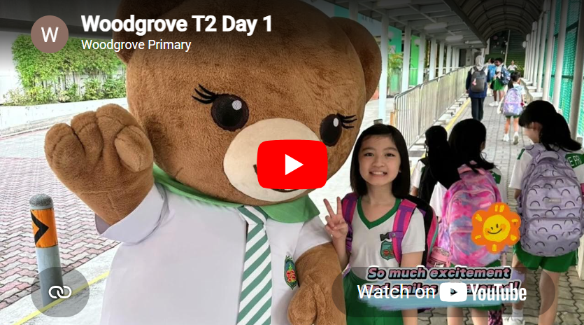 Girl in school uniform poses with teddy bear mascot on covered walkway; other students with backpacks behind.